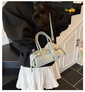 Light blue denim texture pillow bag with bow detail and metal eyelets shown on a shoulder