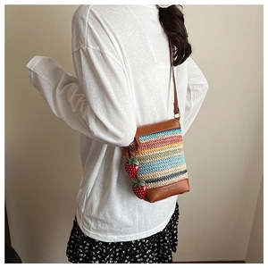 Detail of rainbow woven straw bag featuring leather trim and cute strawberry pendants