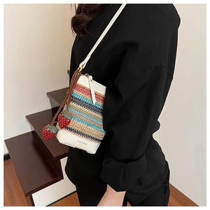 Détail du sac seau en paille à rayures colorées avec base en cuir et breloques fraises