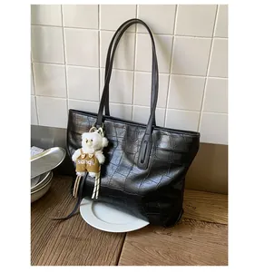 Detail of black crocodile pattern tote bag with a cute plush bear charm on wooden table
