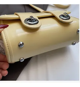 Dettaglio borsa in pelle lucida giallo crema con piedini metallici e chiusura argentata
