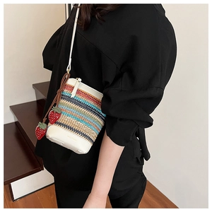 Détail d'un sac seau en paille tressée multicolore avec bordure en cuir blanc et breloque