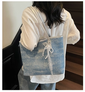 Detail of light blue textured tote bag with lace bow and pearl tassel on shoulder