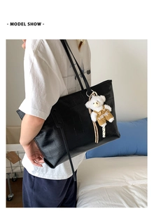 Black crocodile embossed tote bag with teddy bear charm shown on model's shoulder