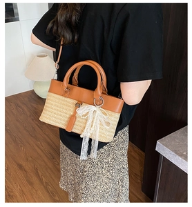 Detail of straw woven tote with brown leather trim, white lace bow, and pearl charm detail