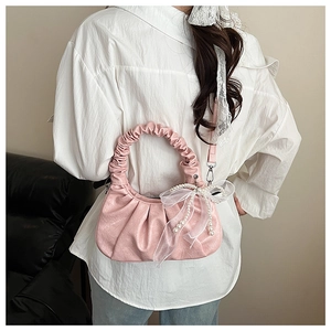 Détail d'un sac nuage plissé rose avec nœud en dentelle et chaîne de perles sur sofa
