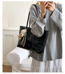 Detail of black faux leather tote with crocodile texture and cute bear pendant