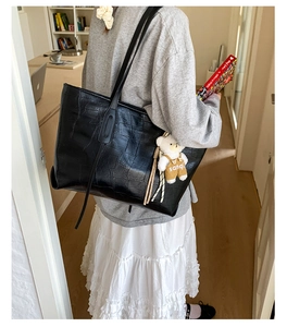 Detail view of black crocodile pattern tote bag with a cute plush bear pendant accessory