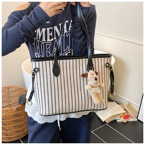 Detail of striped canvas tote bag with leather handles and cute plush dog pendant