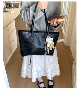 Detail of black crocodile texture tote bag with a white plush bear charm accessory