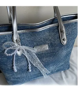 Dettaglio borsa tote in denim blu con manici argento e ciondolo a fiocco