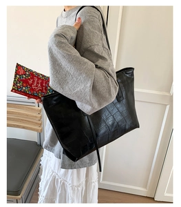 Close-up of black crocodile embossed tote bag texture with minimalist shoulder strap