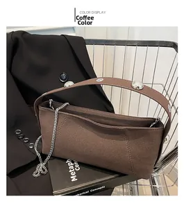 Detail of coffee brown suede underarm bag with silver studs and chain in a basket