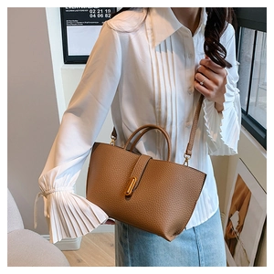 Detail of a brown textured leather tote bag featuring gold buckle and detachable strap