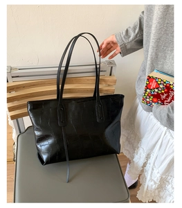 Detail of black faux leather tote bag with crocodile pattern resting on a chair