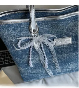 Dettaglio borsa tote in denim blu con finiture in pelle argento, fiocco in pizzo e perle