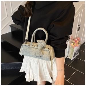Detail view of light blue denim handbag featuring a large bow and silver stud accents