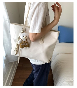 Close-up of white tote bag with crocodile texture and cute plush bear accessory