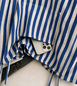 Detail of blue striped tote bag featuring a practical front pocket holding a smartphone