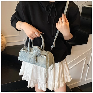 Blue denim pillow bag with rhinestone bow detail worn by a model in casual style