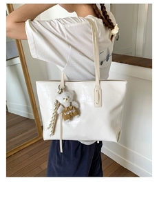 Detail of white crocodile pattern tote bag with cute bear pendant worn on shoulder