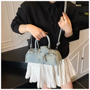 Detail of light blue denim pillow bag featuring a bow, metal studs and chain strap