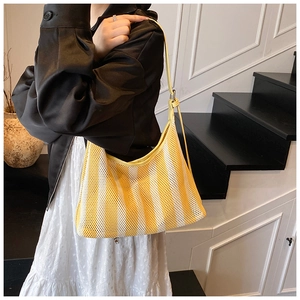 Détail d'un sac hobo en maille rayée jaune avec bandoulière en cuir sur un escalier