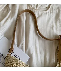 Détail du sac cabas en paille tissée avec anses en cuir marron et coutures fines