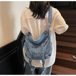 Detail of vintage blue denim crossbody tote bag with cargo pockets and distressed accents