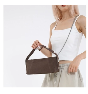 Detail of dark brown suede baguette bag featuring large silver rivets and metal chain strap