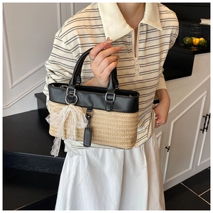 Close-up of straw tote bag with black leather handles and white lace bow accessory
