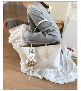 Detail of white crocodile pattern tote bag with a cute plush bear charm decoration