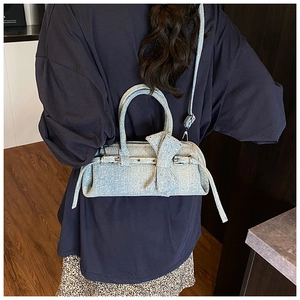 Close-up of light blue denim baguette bag featuring a large bow and metallic buckle details