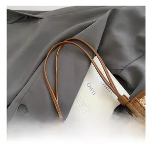 Detailed close-up of woven straw tote bag with slim dark brown leather handles and card