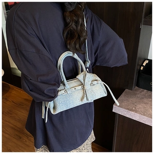 Detail of light blue denim pillow bag featuring metal buckle and oversized bow decor