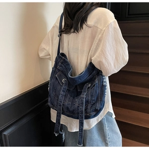 Detail of a large denim crossbody bag with pockets and metal ring on a shoulder strap