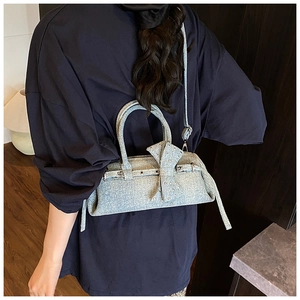 Detail of light blue denim pillow bag with oversized bow and metallic punk eyelets