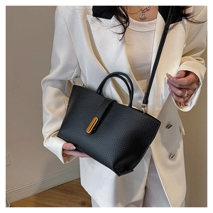 Close-up of black lychee-textured tote bag with gold metal buckle on a white suit model