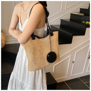 Detail of woven straw tote bag with black faux leather trim and round pendant decoration