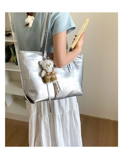 Detail of silver crocodile-textured tote bag with a white plush bear charm on side