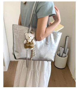 Silver tote bag with crocodile texture and cute plush bear charm detail shown on shoulder