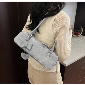 Détail du sac baguette gris à motif crocodile avec nœud en cuir et pendentif en cœur