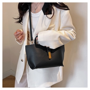 Detail of black lychee grain leather tote bag with gold oval buckle shown on a model