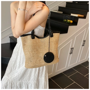 Detail of straw woven tote bag featuring black leather trim and round decorative pendant
