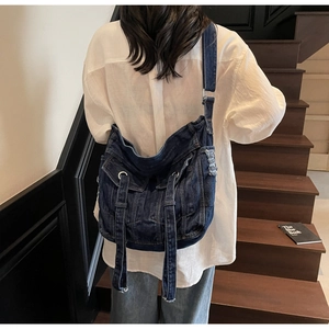 Detail shot of large dark blue denim crossbody bag with jacket pocket design and long straps
