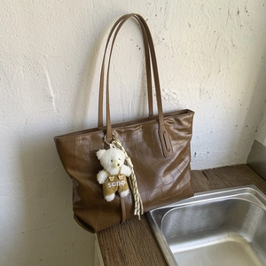 Close-up of brown crocodile texture tote bag featuring a cute teddy bear charm