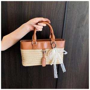 Close-up of woven straw tote with brown PU leather trim and a pearl lace bow charm