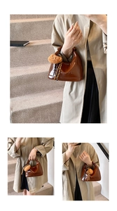 Macro detail of brown patent leather hobo bag with embossed logo and fuzzy ball charm