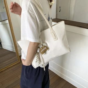 Close-up of a white tote bag with crocodile embossing and a cute bear charm accessory