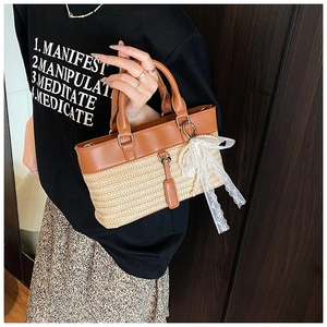 Close-up of woven straw tote bag with brown leather trim and white lace bow detail